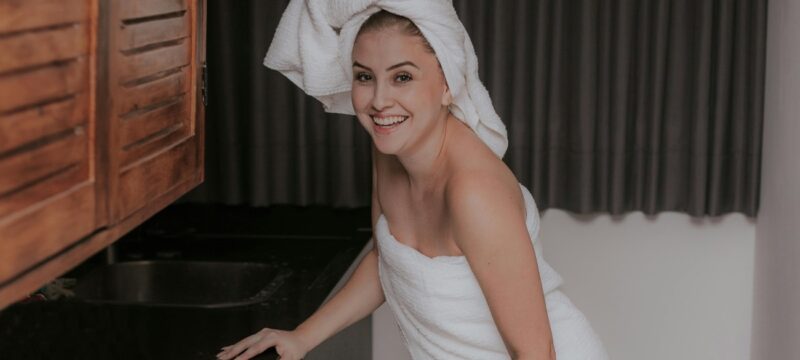 Woman wrapped in towel near sink.