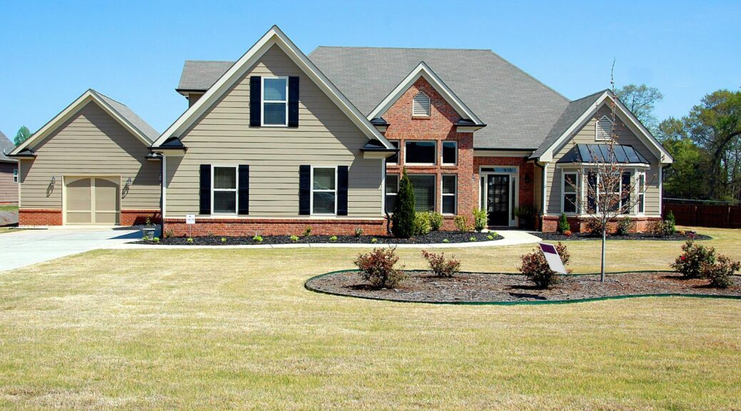 Tan house with green lawn and trees.