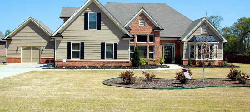 Tan house with green lawn and trees.