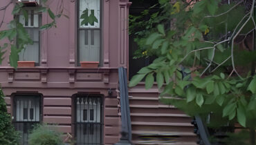 Brownstone building with stairs and green foliage.